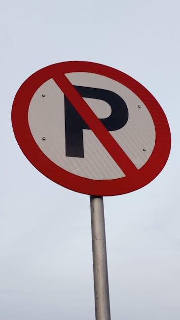 A circular roadside sign with a white background, featuring a bold black letter 'P' crossed out by a red diagonal line within a red border, indicating no parking zone. The sign is mounted on a grey metal pole, set against an overcast sky with grey clouds. In the context of house removals in Lambeth, [COMPANY_NAME] facilitates furniture transport and loading processes, often working around such parking restrictions to ensure efficient home relocation services in the Kennington area, as outlined in the Lambeth council parking rules for Kennington removals.
