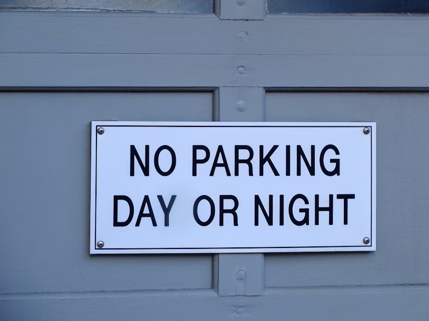 A circular roadside sign with a white background, featuring a bold black letter 'P' crossed out by a red diagonal line within a red border, indicating no parking zone. The sign is mounted on a grey metal pole, set against an overcast sky with grey clouds. In the context of house removals in Lambeth, [COMPANY_NAME] facilitates furniture transport and loading processes, often working around such parking restrictions to ensure efficient home relocation services in the Kennington area, as outlined in the Lambeth council parking rules for Kennington removals.